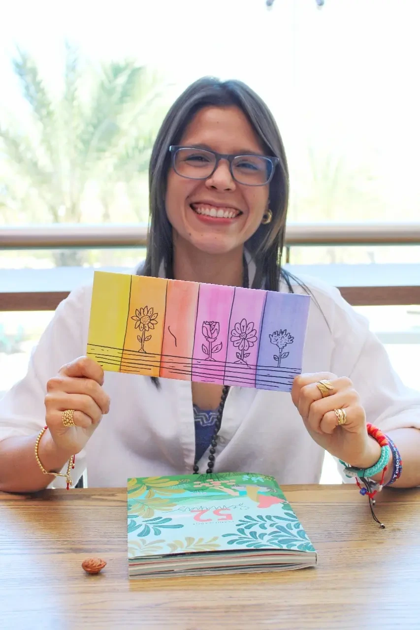 Gaby sostiene tarjetas ilustradas con flores en distintas etapas.