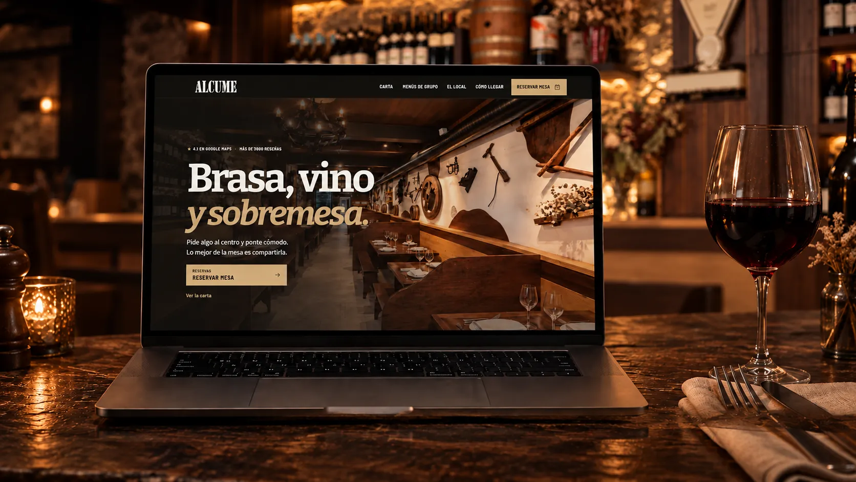 Presentación de la web de Alcume en un portátil, con una copa de vino y la bodega de piedra y madera al fondo.