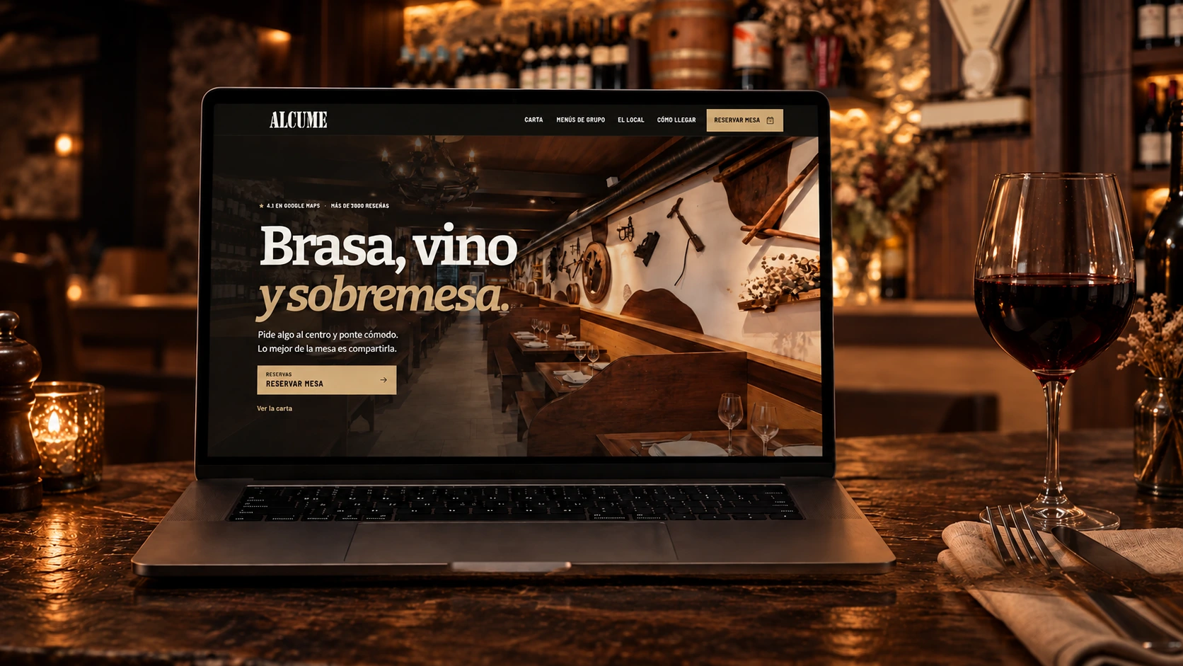 Presentación de la web de Alcume en un portátil, con una copa de vino y la bodega de piedra y madera al fondo.