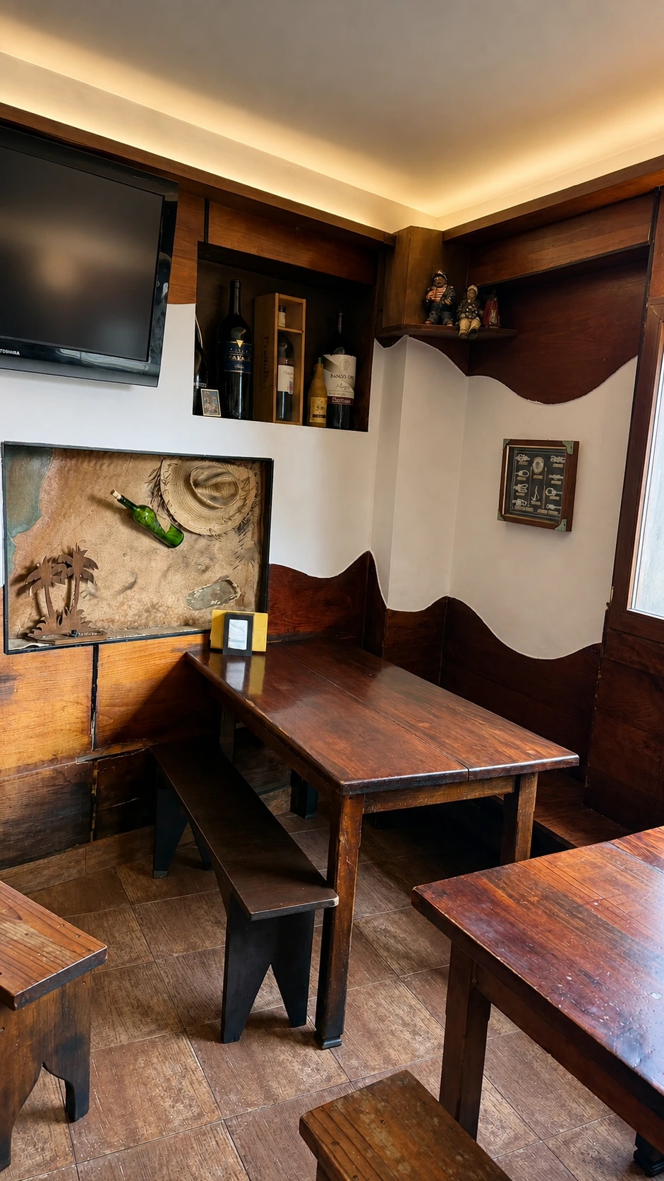 Rincón interior de La Taberna del Chipirón con mesas de madera y pared ondulada.